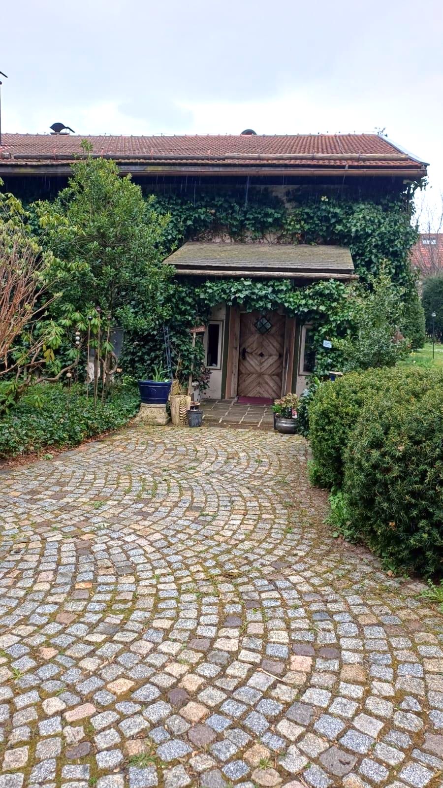Haustür des Scharamer Hofs unter efeubewachsenem Vordach, davor der Hof aus Kopfsteinpflaster
